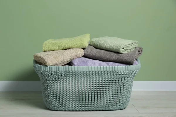 Plastic laundry basket with clean terry towels on floor near light green wall