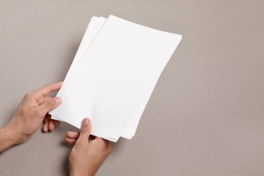 Man holding sheets of paper on grey background, closeup. Mockup for design
