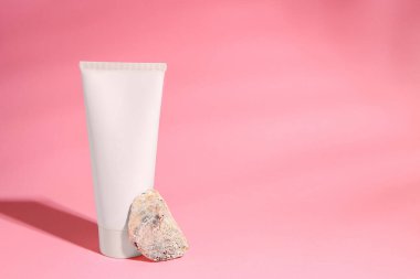 Tube of cream and stone on pink background. Space for text