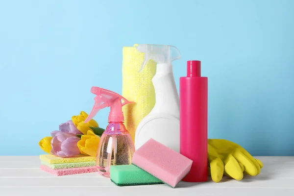 Spring cleaning. Detergents, flowers and sponges on white wooden table against light blue background
