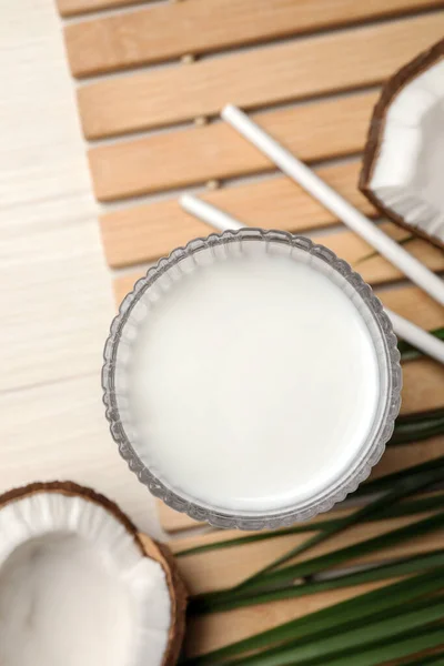 Glass of delicious vegan milk and coconuts on white wooden table, flat lay