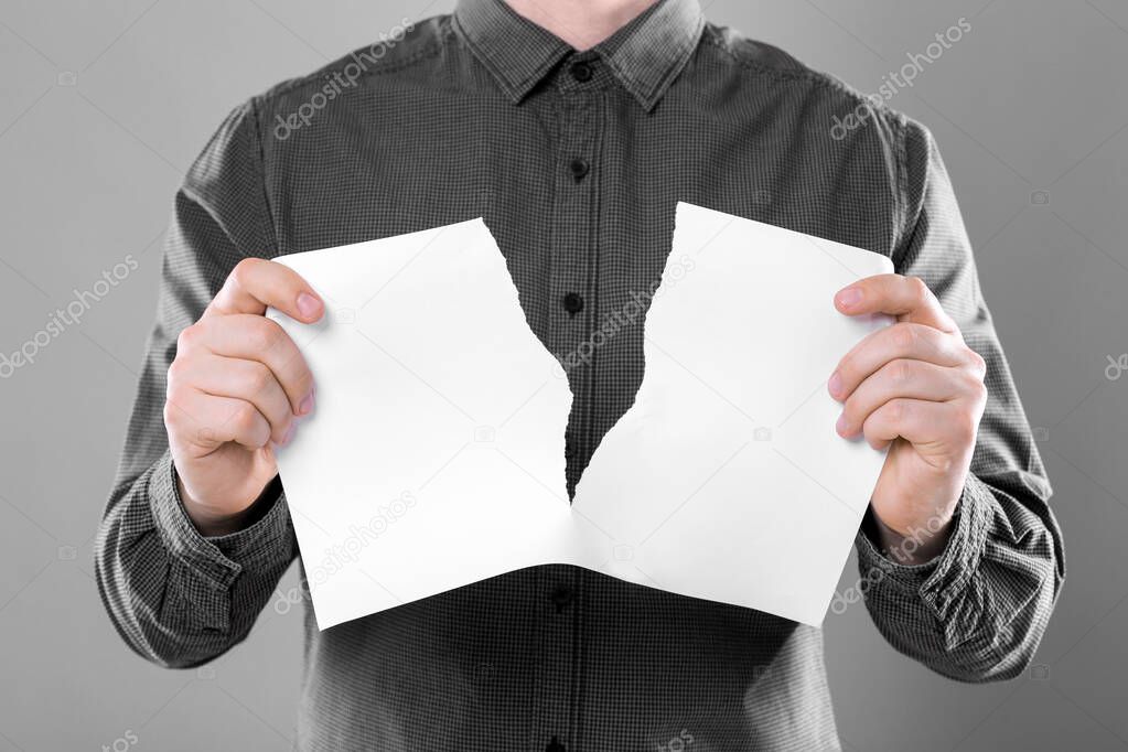 Man ripping sheet of paper on grey background, closeup. Mockup for design
