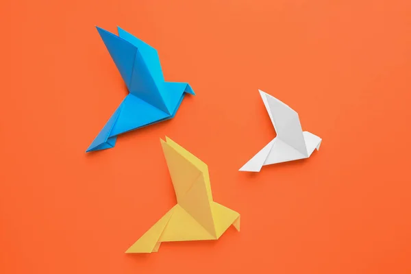 Beautiful colorful origami birds on orange background, flat lay