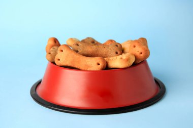 Bone shaped dog cookies in feeding bowl on light blue background