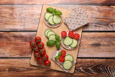 Tasty crispbreads, cucumber, tomatoes and basil on wooden table, flat lay