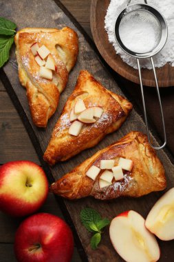 Fresh tasty puff pastry with sugar powder, mint and apples served on wooden table, flat lay