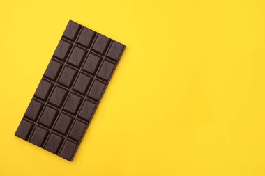 Tasty chocolate bar on yellow background, top view. Space for text