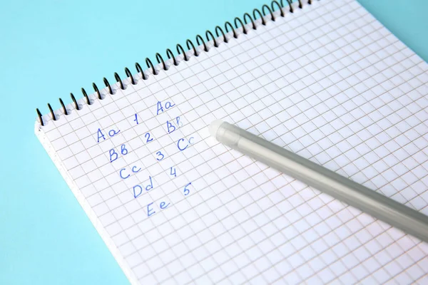 Letters and numbers written in notepad with erasable pen on light blue background, closeup