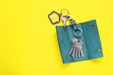 Open leather holder with keys on yellow background, top view. Space for text