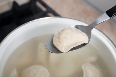 Spoon with tasty dumpling (varenyk) over pot indoors, closeup