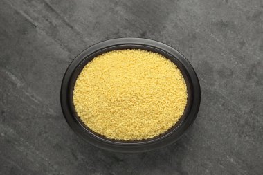 Bowl of raw couscous on grey table, top view