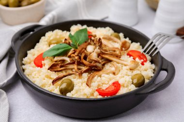 Tasty couscous with mushrooms, olives and tomatoes served on grey table, closeup clipart