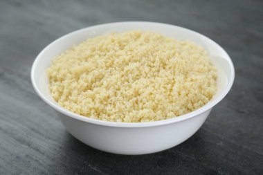 Bowl of tasty couscous on grey table, closeup