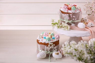 Traditional Easter cakes with meringues and painted eggs on white wooden table, space for text