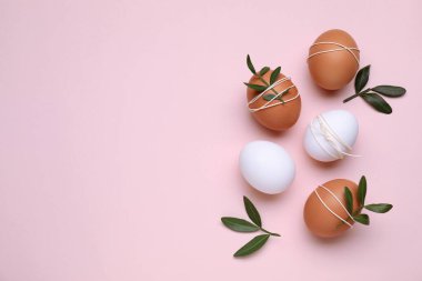 Beautifully decorated Easter eggs and green leaves on pale pink background, flat lay. Space for text