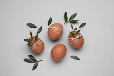 Beautifully decorated Easter eggs and green leaves on light grey background, flat lay