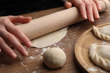 Woman rolling dough for chebureki on wooden table, closeup
