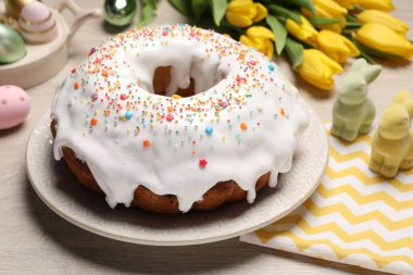 Easter cake with sprinkles, decorative bunnies, painted eggs and tulips on white wooden table