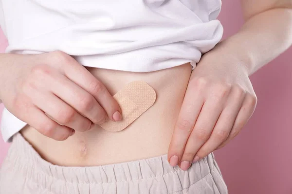 Woman applying contraceptive patch onto her body on pink background, closeup