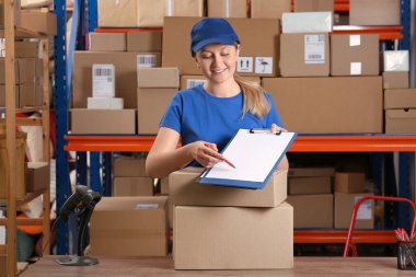 Post office worker with clipboard and parcels near rack indoors