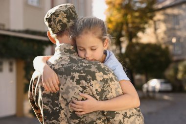 Daughter hugging her father in Ukrainian military uniform outdoors. Family reunion
