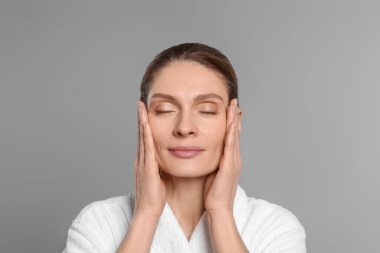 Woman massaging her face on grey background