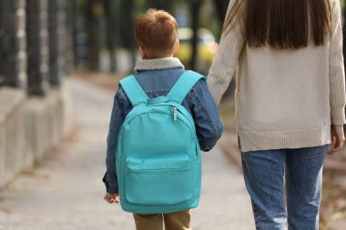 Young mom taking her son to school, back view