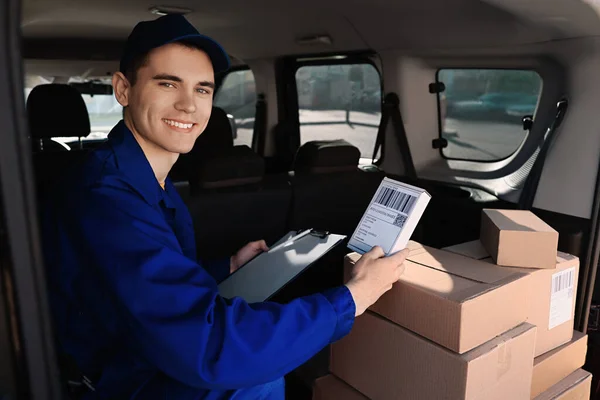Courier with clipboard checking packages in delivery van