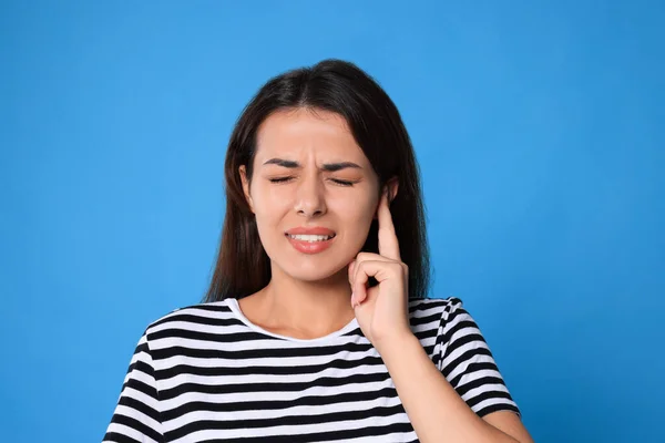 Young woman suffering from ear pain on light blue background
