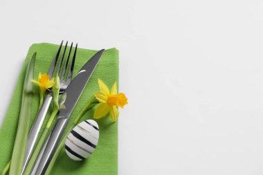 Cutlery set, Easter egg and narcissuses on white background, space for text. Festive table setting