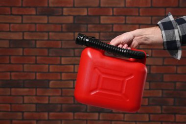 Man holding red canister against brick wall, closeup. Space for text