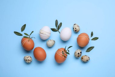 Beautifully decorated Easter eggs and green leaves on light blue background, flat lay