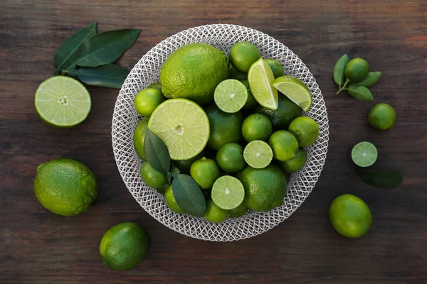 Fresh ripe limes and green leaves on wooden table, flat lay