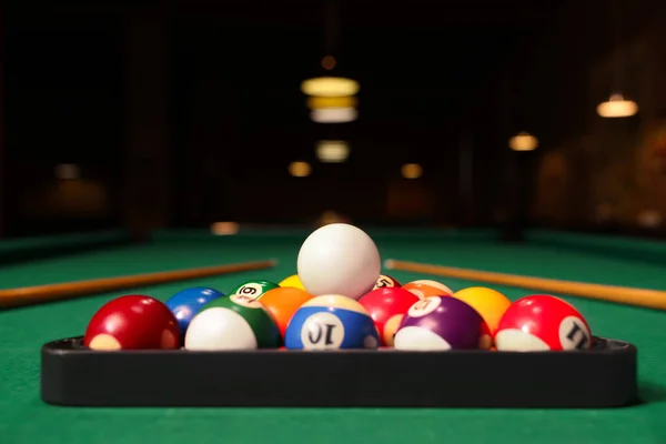 Plastic triangle rack with billiard balls and cues on green table indoors, space for text