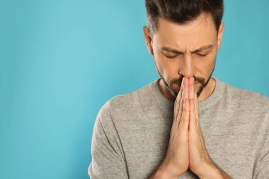 Man with clasped hands praying on turquoise background. Space for text