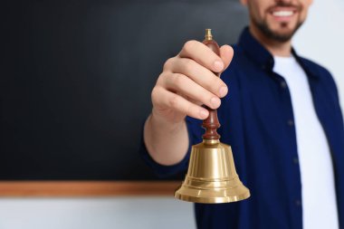 Teacher with school bell near black chalkboard, closeup. Space for text