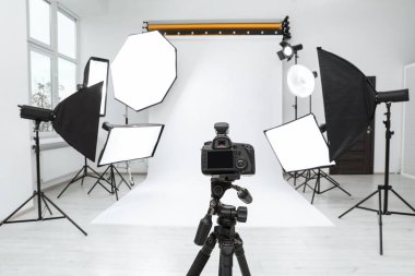 Tripod with camera and professional lighting equipment in modern photo studio