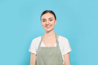 Beautiful young woman in clean apron with pattern on light blue background