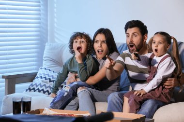 Surprised family watching TV with pizza on sofa at home