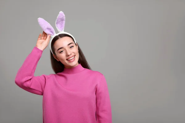 Happy woman wearing bunny ears headband on grey background, space for text. Easter celebration
