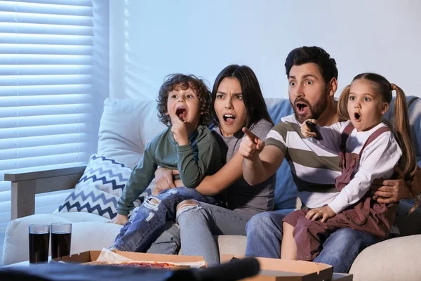 Surprised family watching TV with pizza on sofa at home