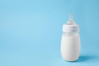 One feeding bottle with milk on light blue background. Space for text