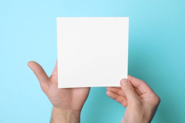 Man holding sheet of paper on light blue background, top view. Mockup for design