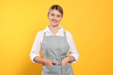 Beautiful young woman in clean apron with pattern on orange background