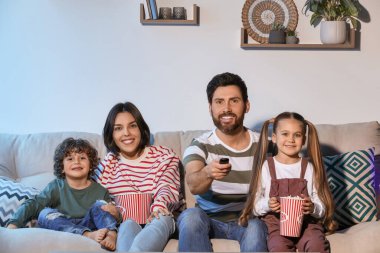 Happy family watching TV with popcorn on sofa indoors