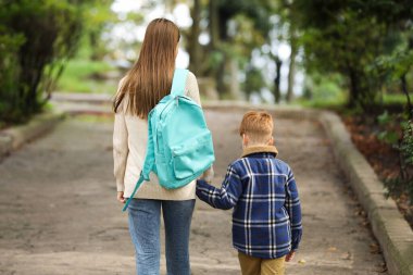 Young mom taking her son to school, back view