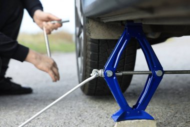 Man changing car tire, focus on scissor jack outdoors