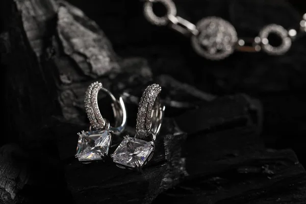 Luxury jewelry. Stylish presentation of elegant earrings on coal, closeup