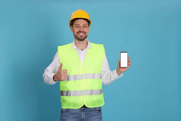 Male industrial engineer in uniform with phone on light blue background