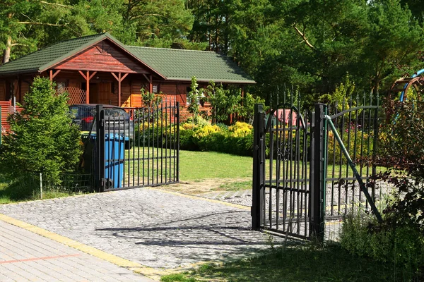Open metal gates near house, trees and bushes outdoors